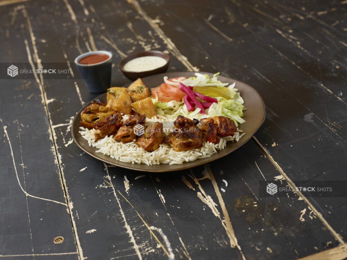 Middle eastern platter with chicken kebab, rice, potatoes and salad with sauces on a distressed wooden background