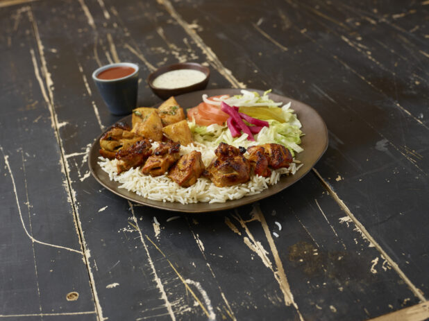 Middle eastern platter with chicken kebab, rice, potatoes and salad with sauces on a distressed wooden background