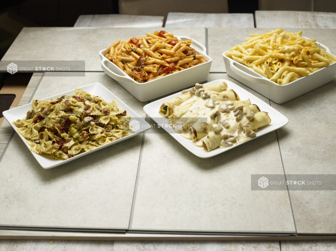 Various catered pastas and stuffed crepes on a tiled background