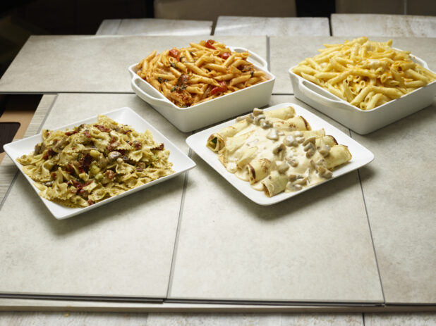 Various catered pastas and stuffed crepes on a tiled background