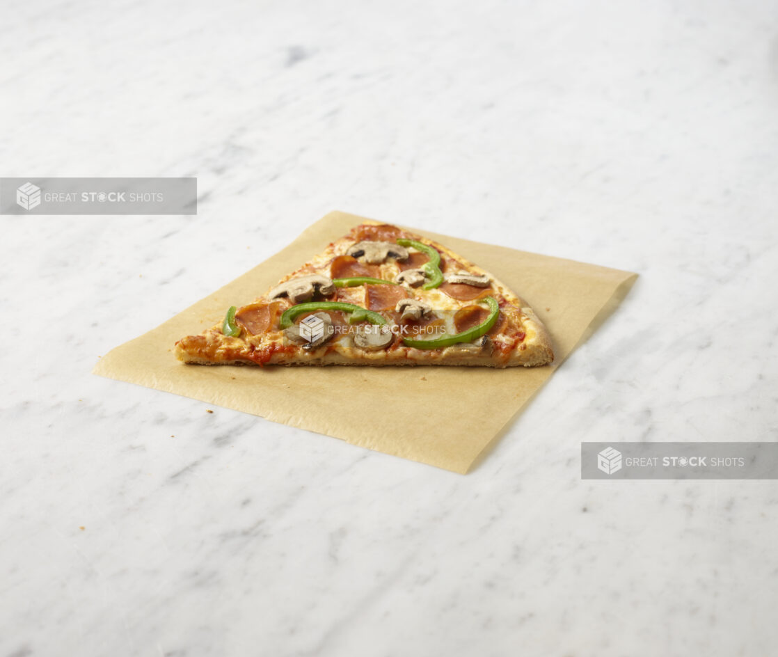 Slice of deluxe pizza on parchment paper sitting on a marble background