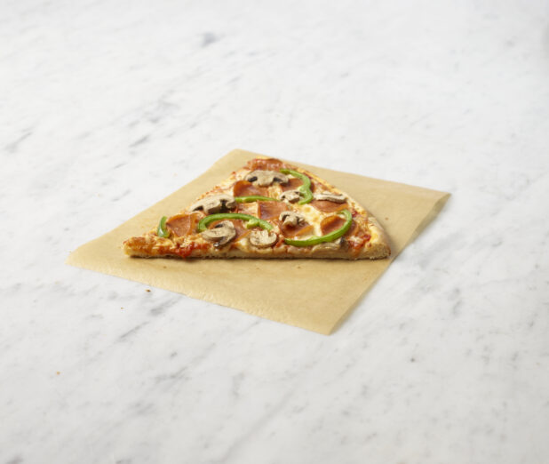 Slice of deluxe pizza on parchment paper sitting on a marble background