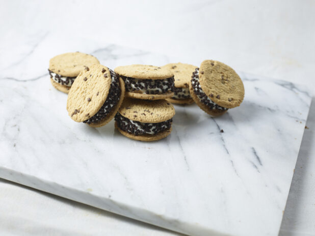 Many chocolate chip ice cream sandwiches stacked on a white marble slab