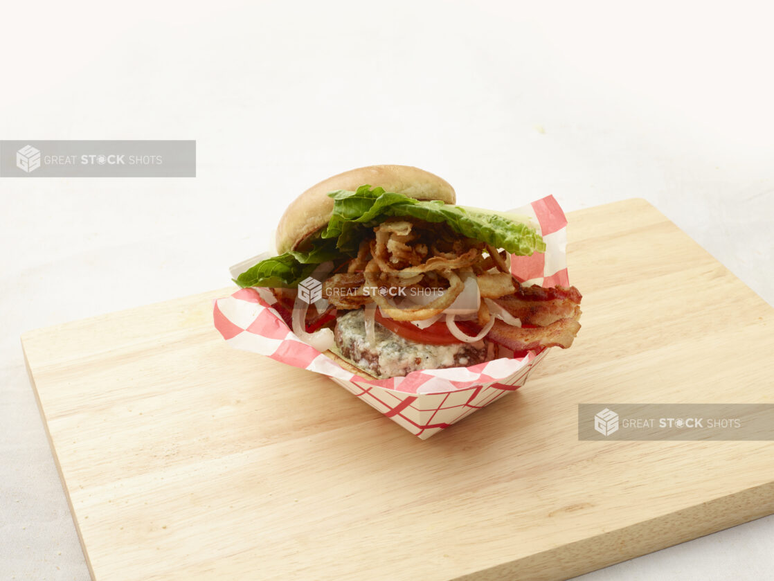 Hamburger with bacon, lettuce, tomato, cheese and shoestring fried onions with a toasted bun on a cutting board