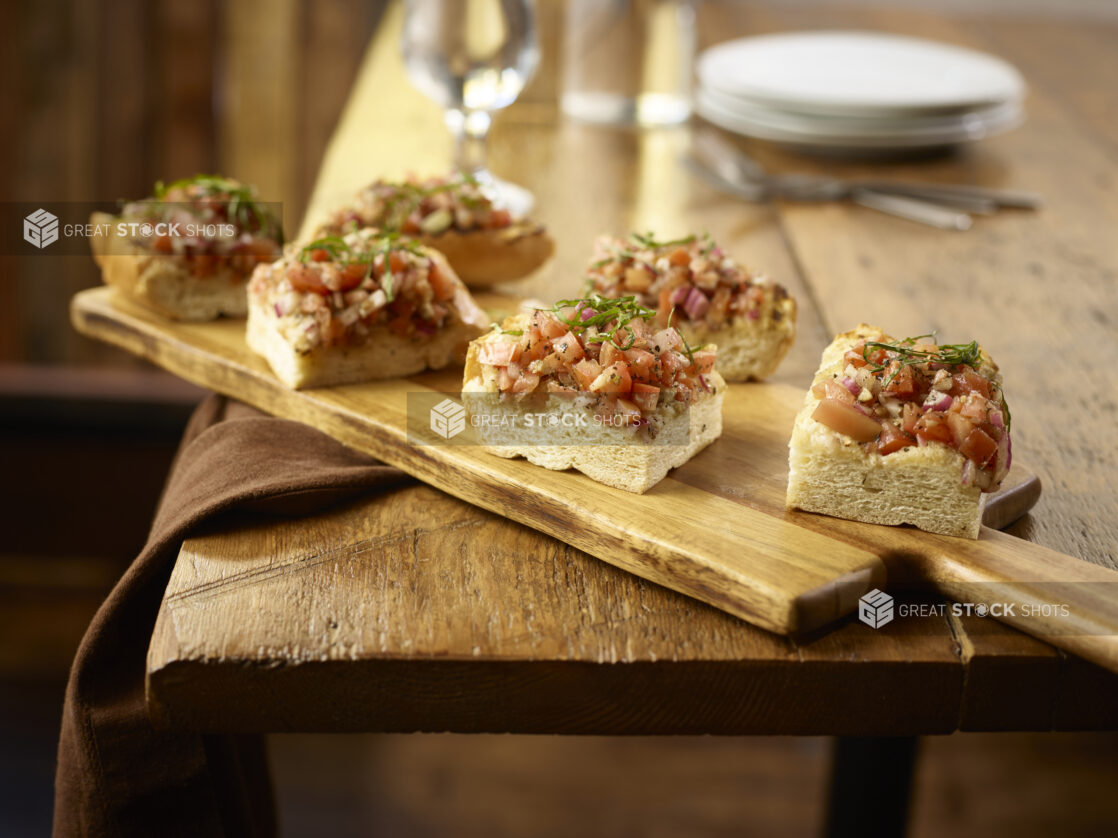 Bruschetta pieces on top of a wooden plank sitting on a wooden table