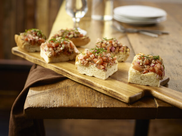 Bruschetta pieces on top of a wooden plank sitting on a wooden table
