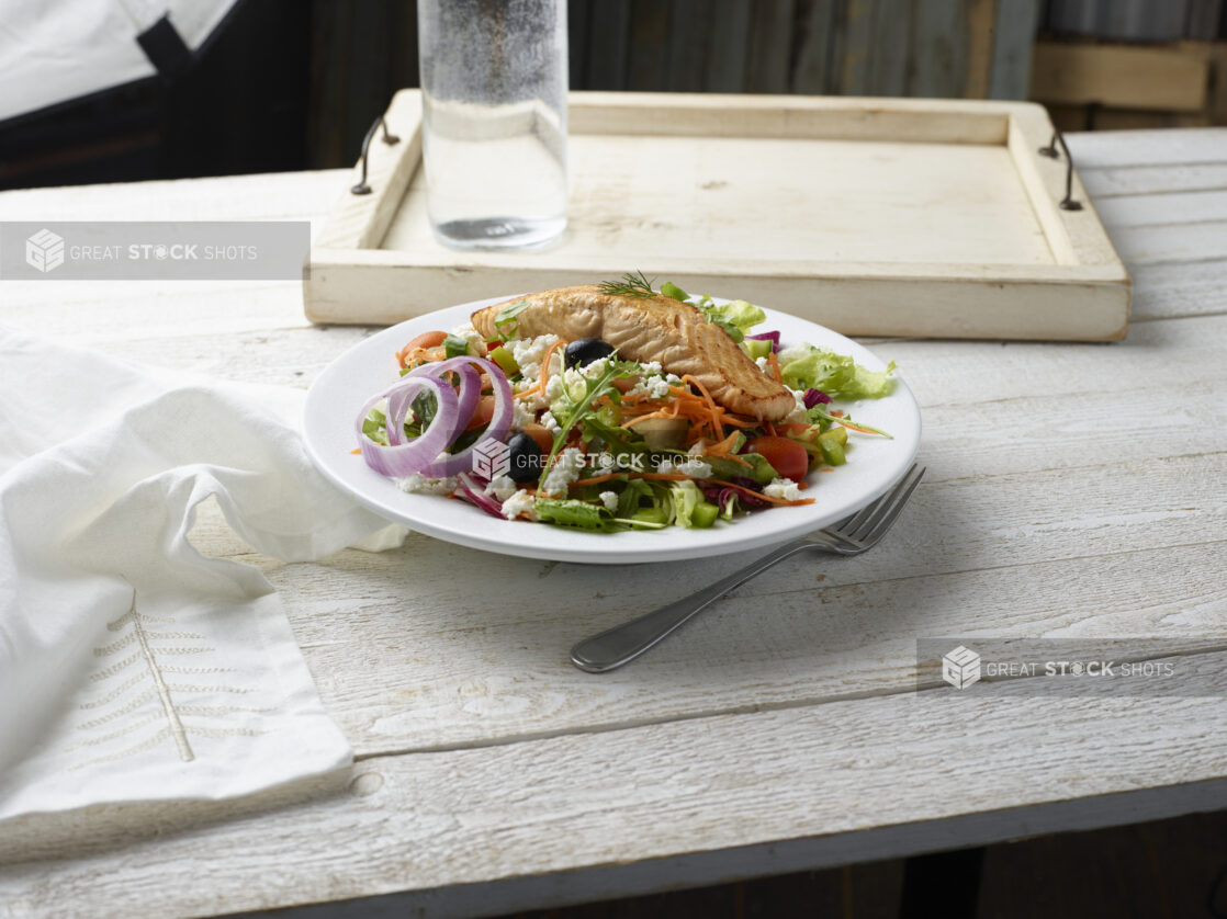 Greek salad with grilled salmon in a white bowl on a whitewashed wooden background,