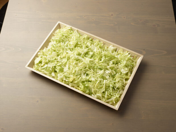 Wood catering tray filled with shredded lettuce, Middle Eastern platter, wood grain background