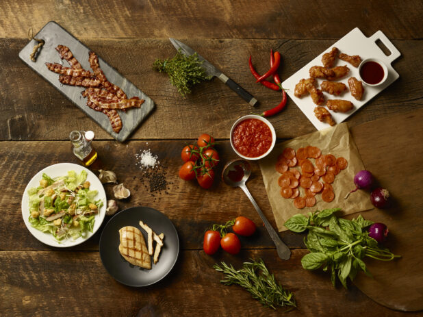 Fresh pizza restaurant ingredients and appetizers on a wooden background, overhead view