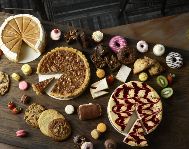Overhead of cakes and other desserts on a dark wooden background, overhead