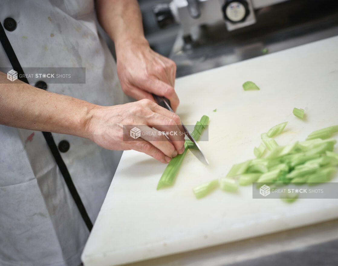 Prep cook chopping celery on a white cutting board, kitchen setting