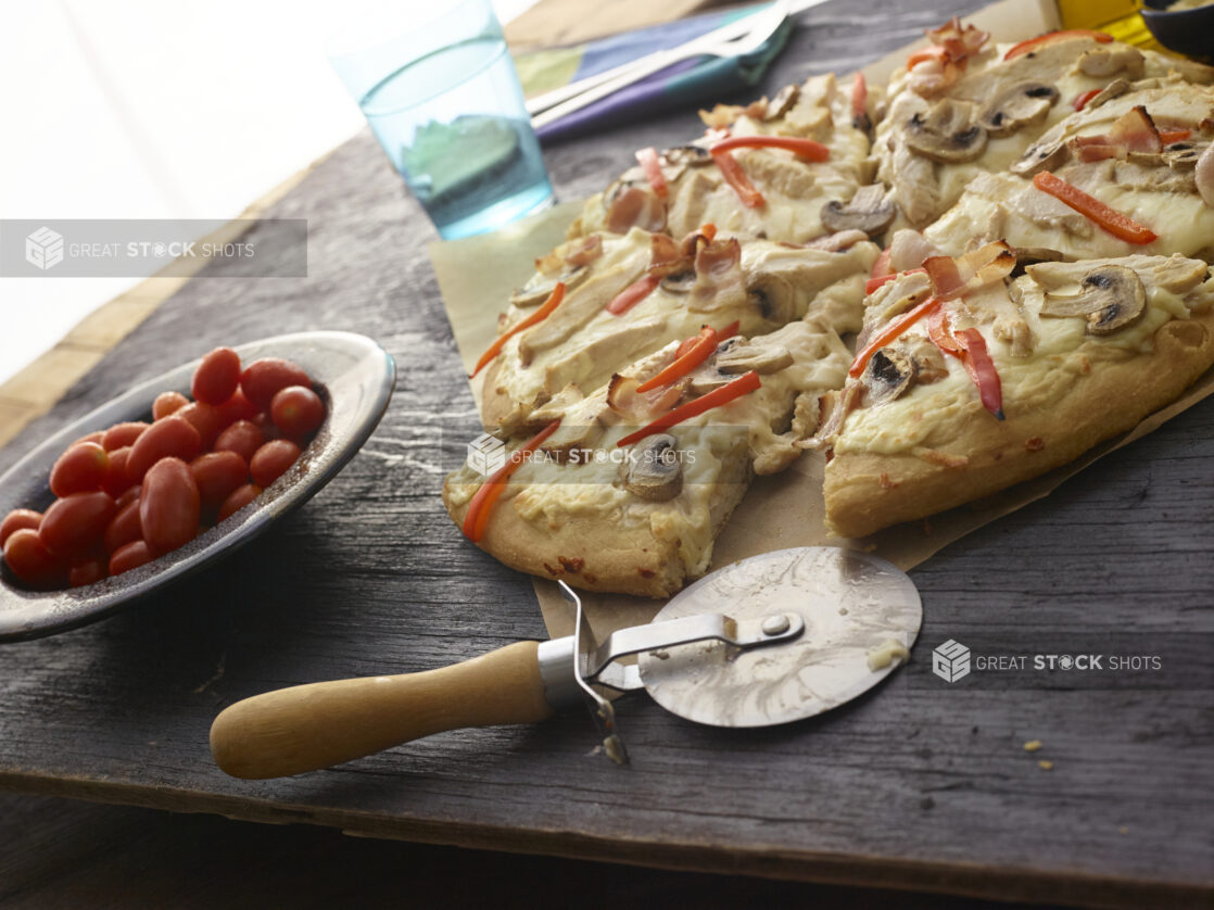 Sliced white pizza with mushrooms, red peppers, chicken, bacon and cheese on dark wooden background