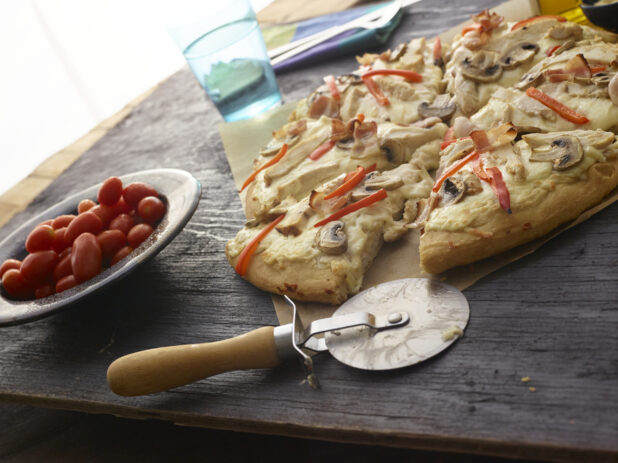Sliced white pizza with mushrooms, red peppers, chicken, bacon and cheese on dark wooden background