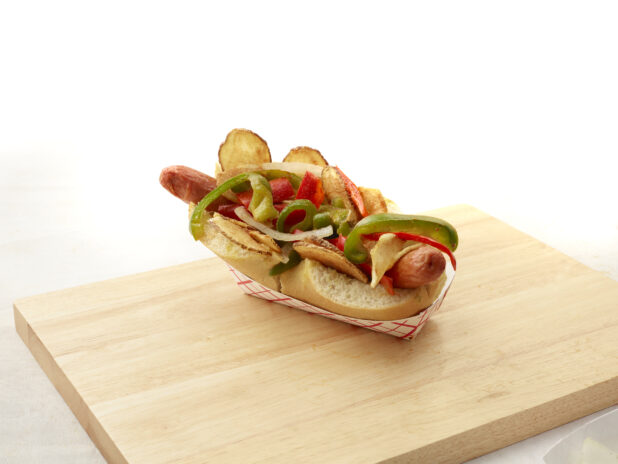 Loaded hot dog with peppers, potato chips and onions on a wooden block