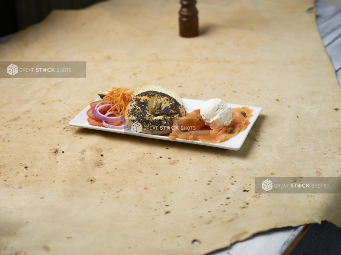 Breakfast plate with poppy seed bagel, salmon, cream cheese and capers on a light background