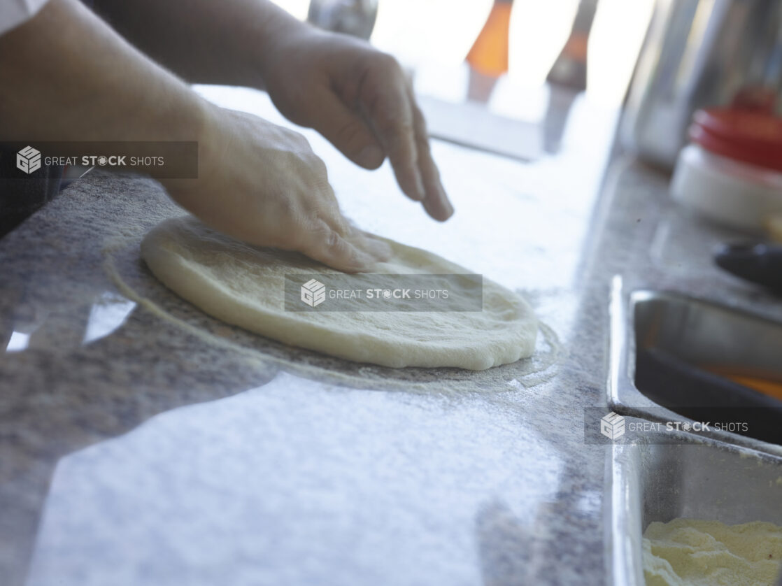 Pizza chef forming a pizza crust on a cornmeal-coated marble work surface