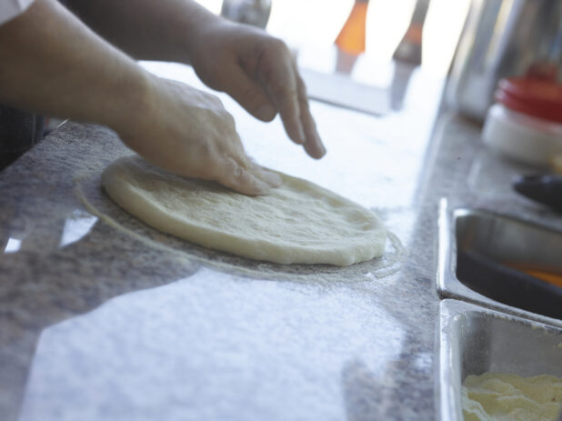 Pizza chef forming a pizza crust on a cornmeal-coated marble work surface