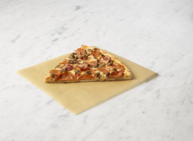 Slice of three meat pizza on parchment paper on a marble background