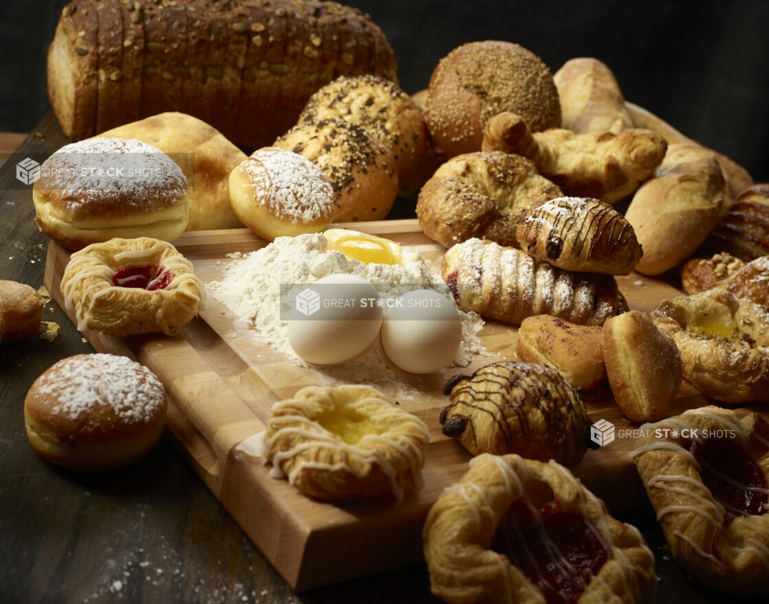 Collection of various desserts / pastries with fresh eggs and flour with an egg well on a wooden block