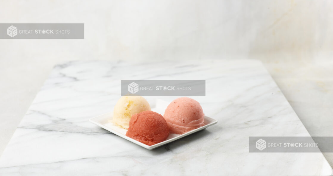 Three scoops of gelato on a square white plate, marble background