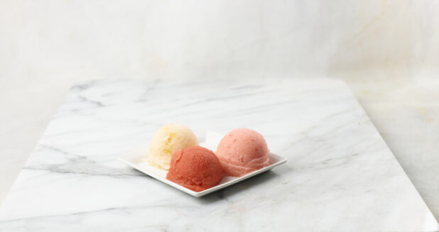 Three scoops of gelato on a square white plate, marble background