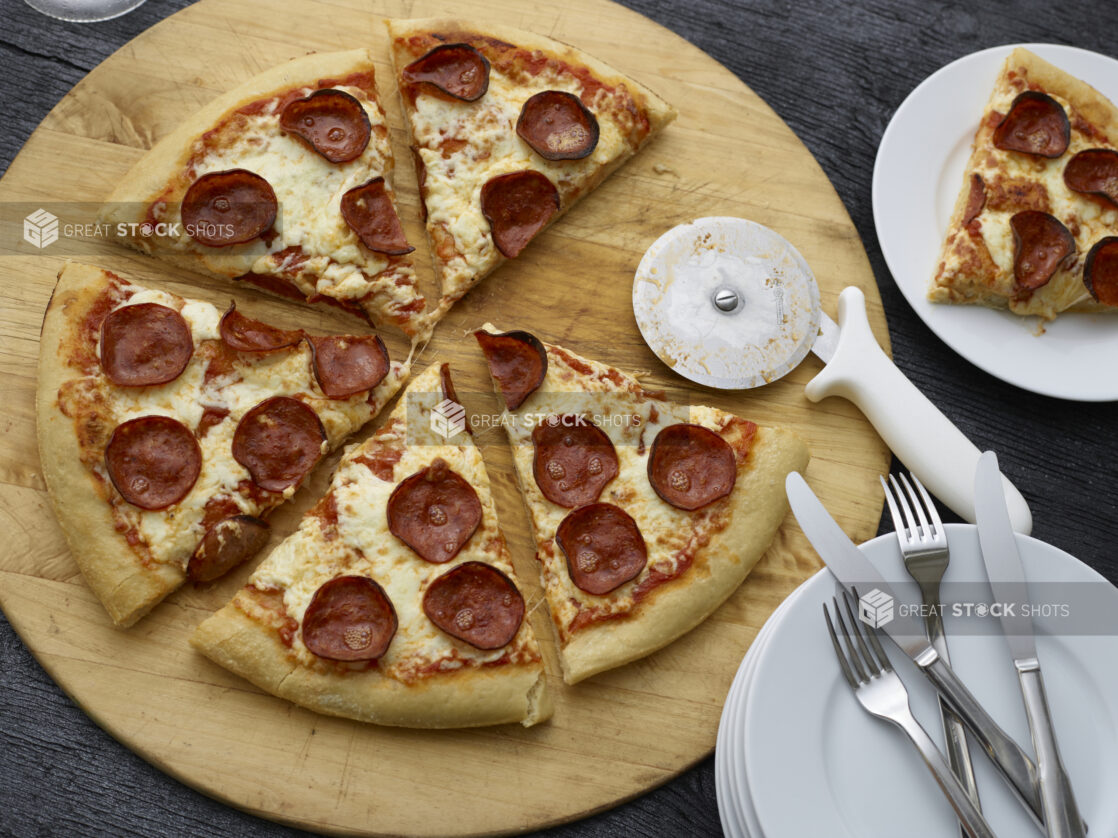 Overhead sliced pepperoni pizza on a wooden cutting board with pizza cutter