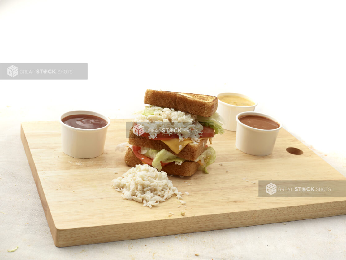 Chopped crab / lobster on a triple-decker sandwich with lettuce, tomato and cheese, on a wooden board