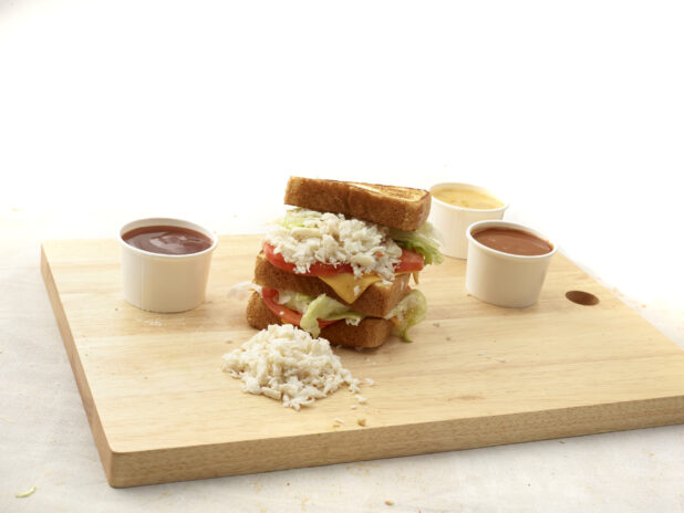 Chopped crab / lobster on a triple-decker sandwich with lettuce, tomato and cheese, on a wooden board