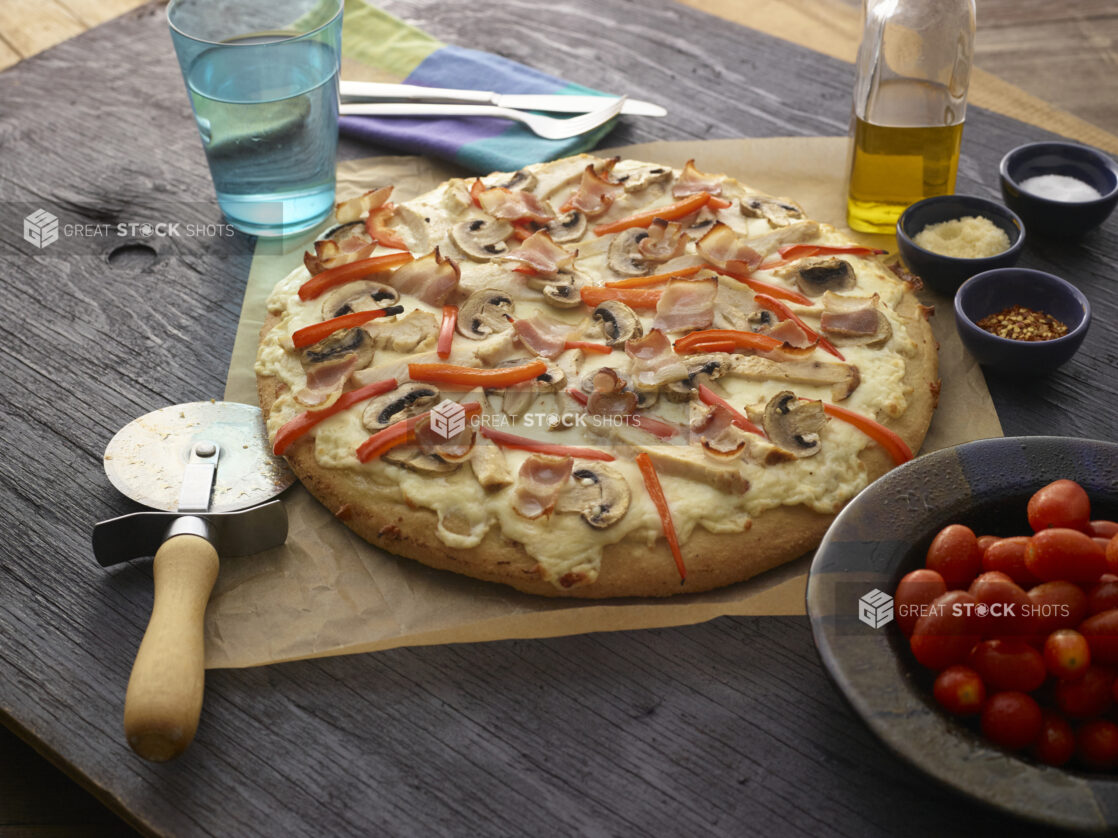 Whole white pizza with mushrooms, red peppers, chicken, bacon and cheese on dark wooden background