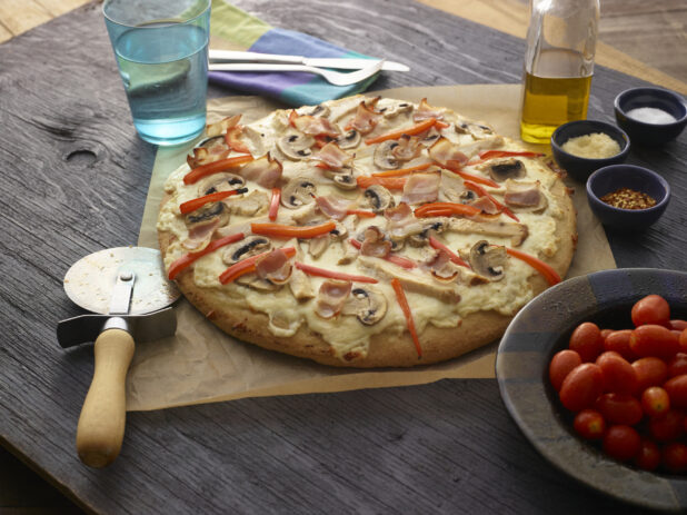 Whole white pizza with mushrooms, red peppers, chicken, bacon and cheese on dark wooden background