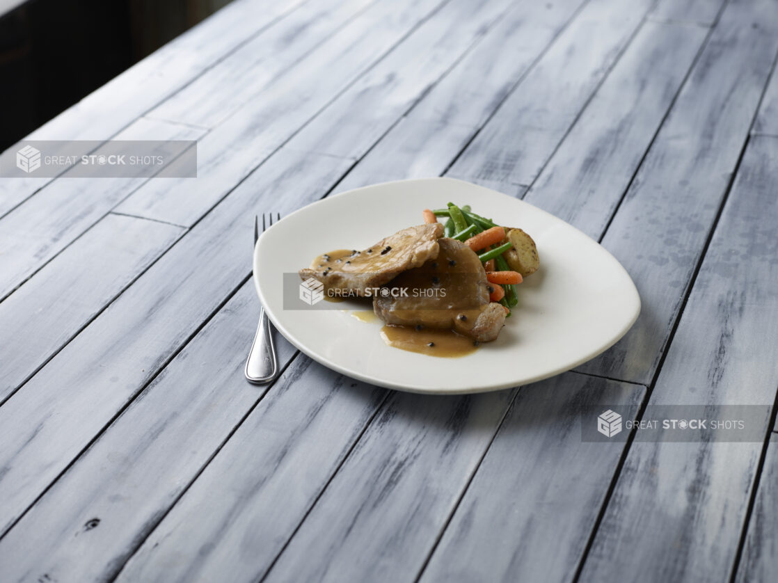 Pork, green beans, baby carrots and roasted potatoes with a peppercorn sauce on a wooden background