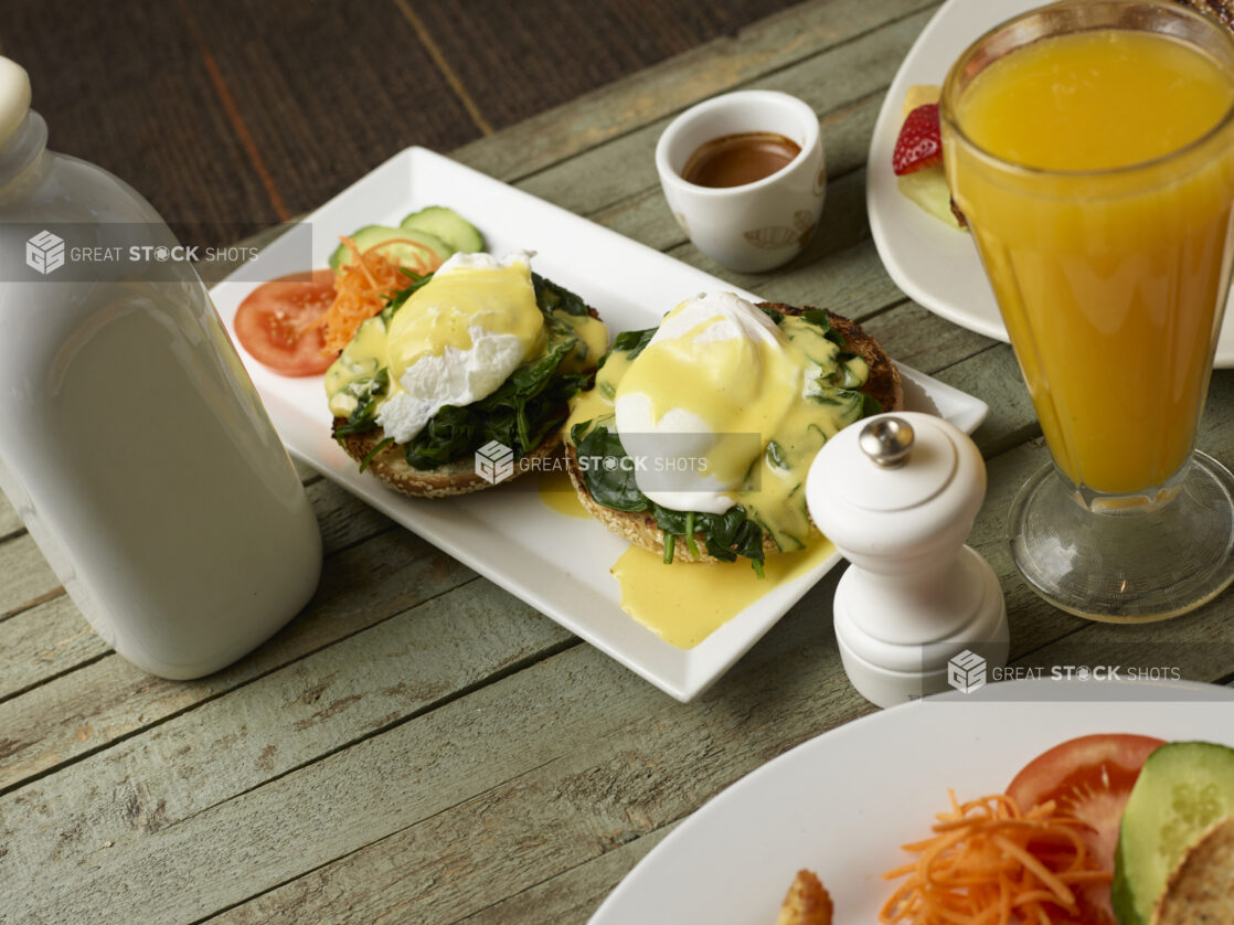 Eggs benedict florentine on white plate with orange juice on a wooden background