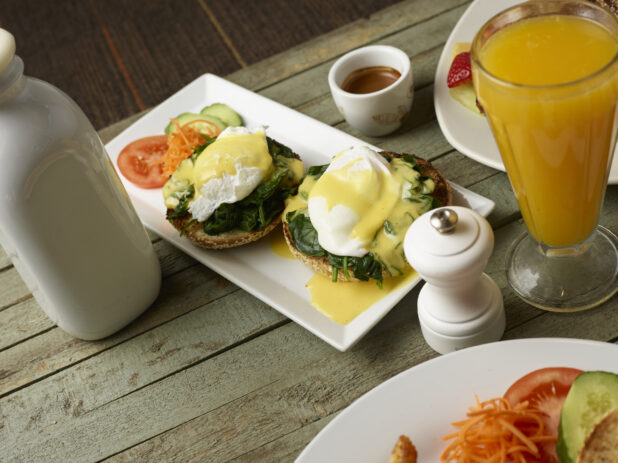 Eggs benedict florentine on white plate with orange juice on a wooden background