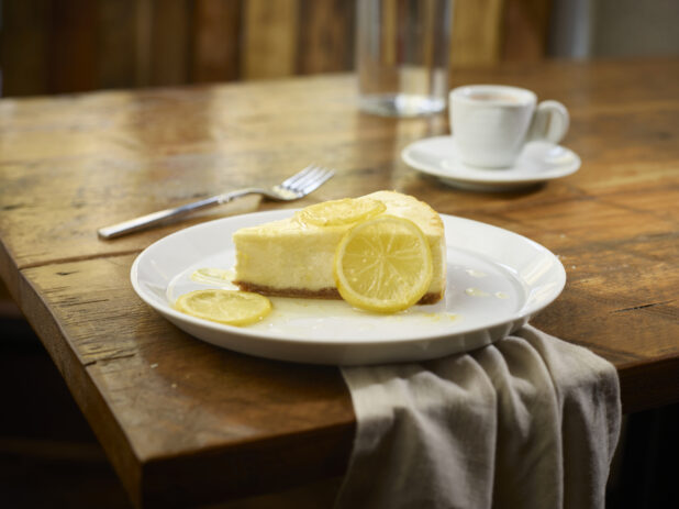 Slice of lemon cheesecake on a wooden table with coffee