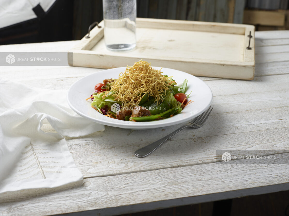 Asian salad with crunchy noodles on top in a white bowl on a whitewashed wood background