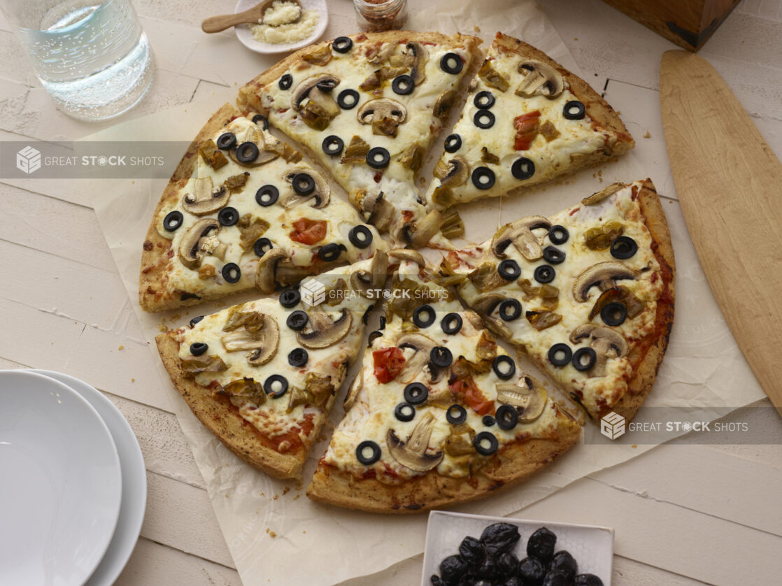 Vegetarian pizza cut into slices on parchment with a white washed wooden background