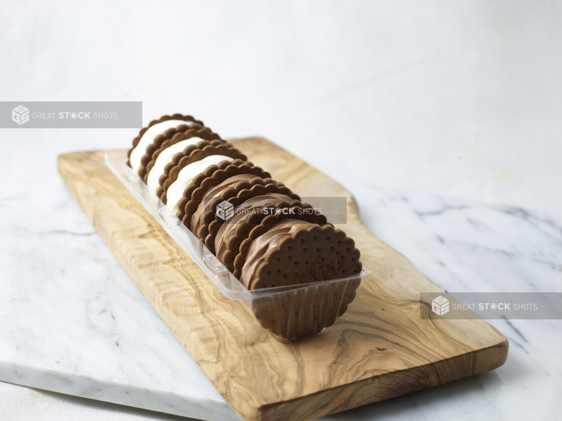 Vanilla and chocolate ice cream sandwiches in a plastic container on a wooden board on a marble slab