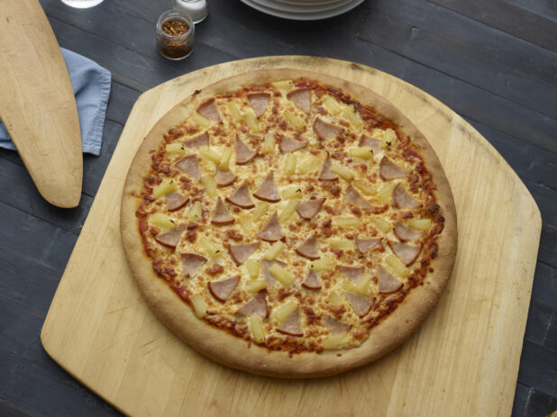 Whole Hawaiian pizza on pizza paddle on a dark wooden background