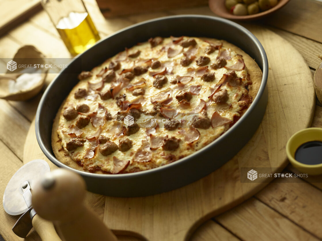 Whole deep dish meat pizza in a pan on a wooden background with ingredients