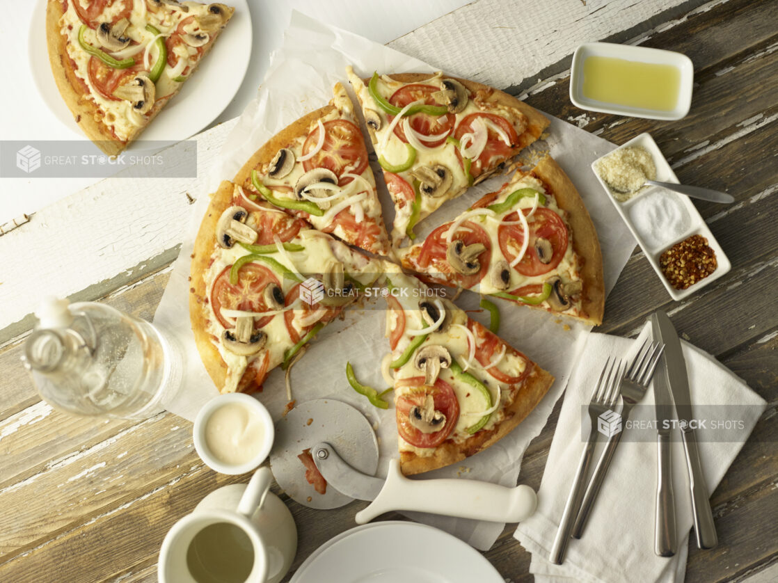 Vegetarian pizza cut into slices on parchment on top of a wooden background