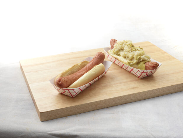 Two hot dogs on a wooden cutting board