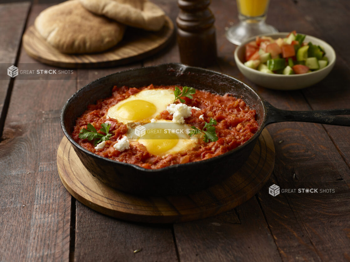 Shakshuka / egg entree made with tomatoes, peppers and onions in a skillet on a wooden background