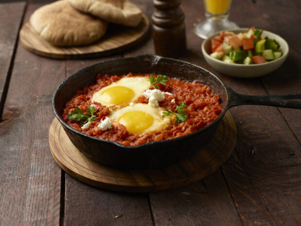 Shakshuka / egg entree made with tomatoes, peppers and onions in a skillet on a wooden background