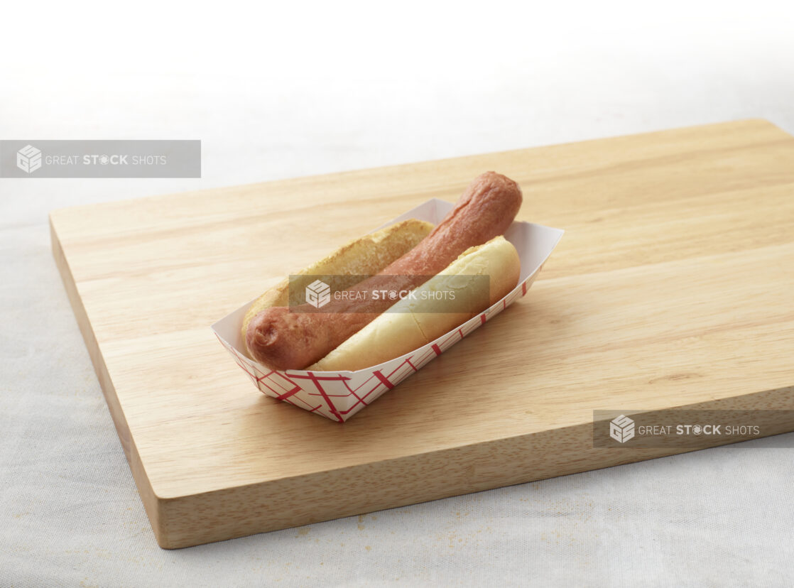 Plain hot dog with bun on a wooden cutting board