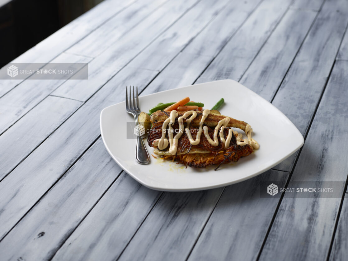 Fine dining entree on white plate with fork on top of a grey wooden background