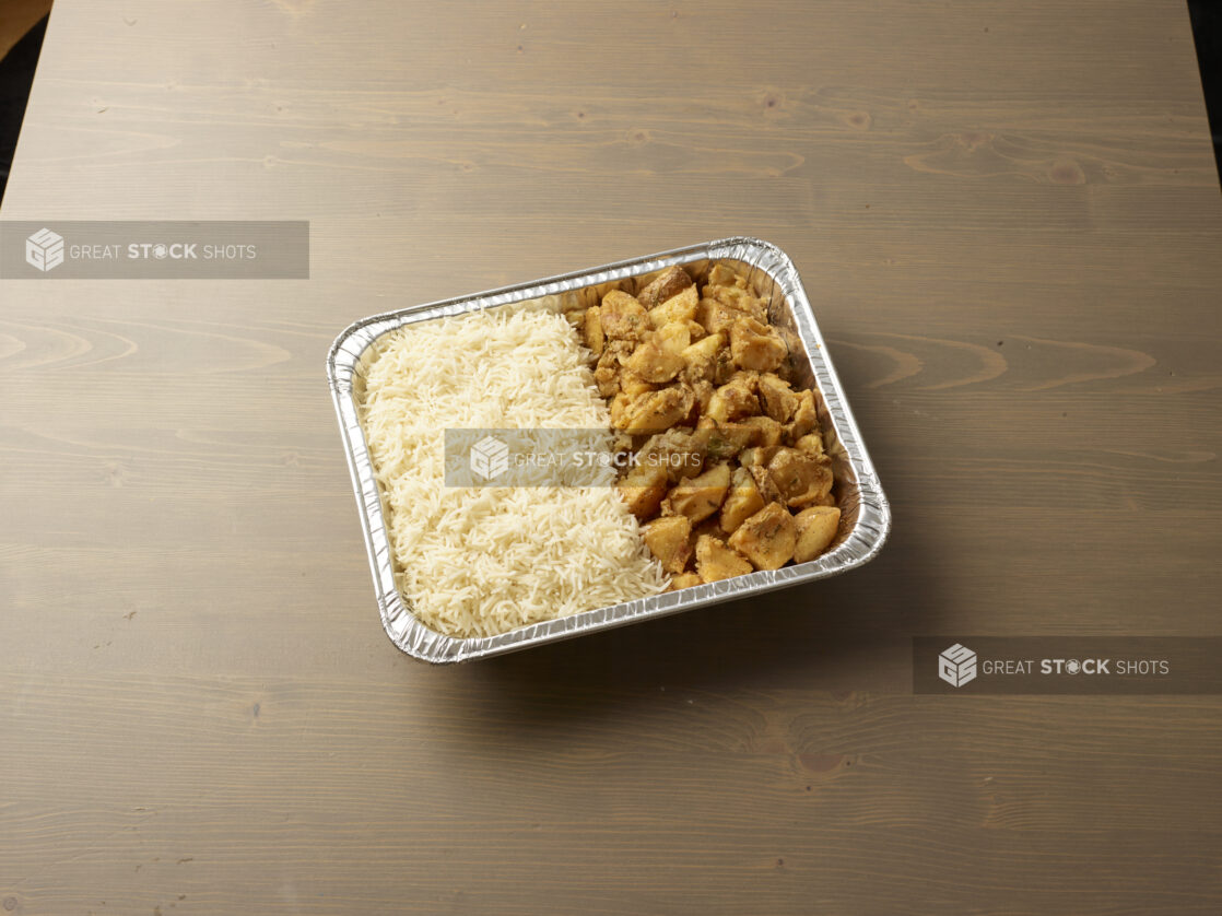 Rice and potatoes in an aluminum foil tray on a wooden table