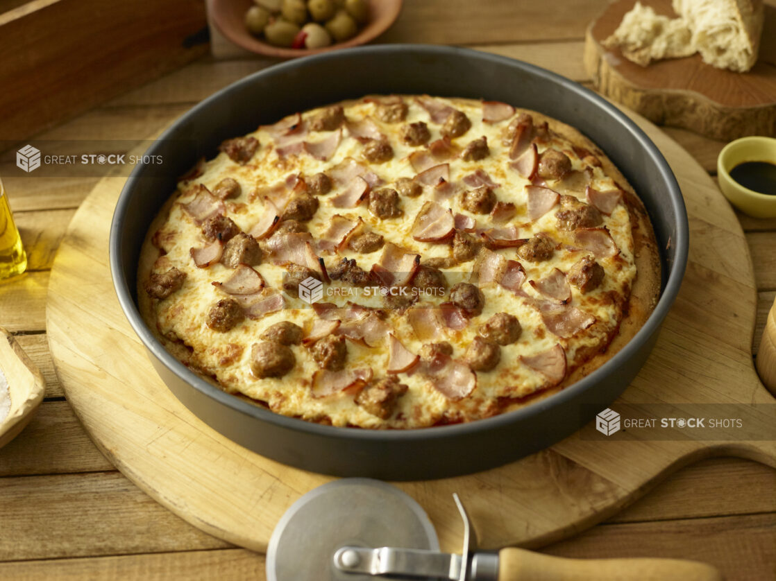 Whole deep dish meat pizza in a pan on a wooden background with ingredients