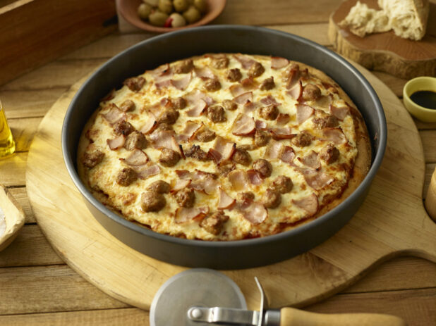 Whole deep dish meat pizza in a pan on a wooden background with ingredients