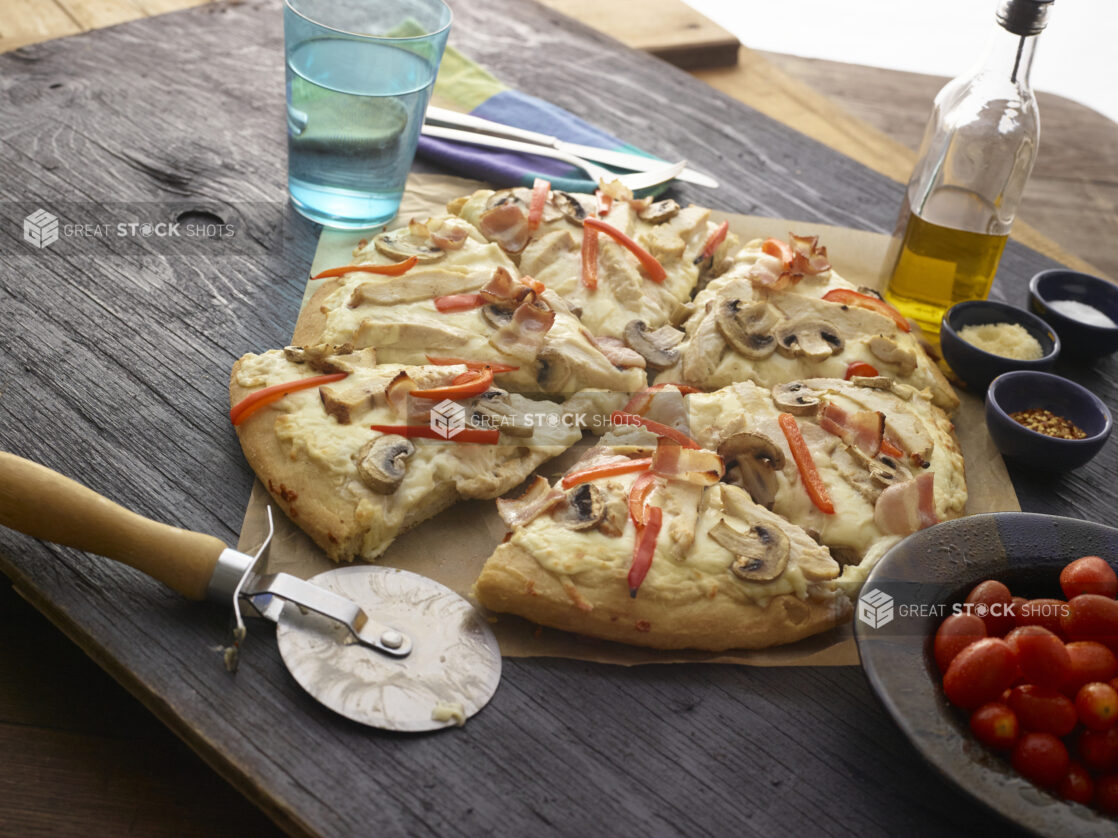 Sliced white pizza with mushrooms, red peppers, chicken, bacon and cheese on dark wooden background