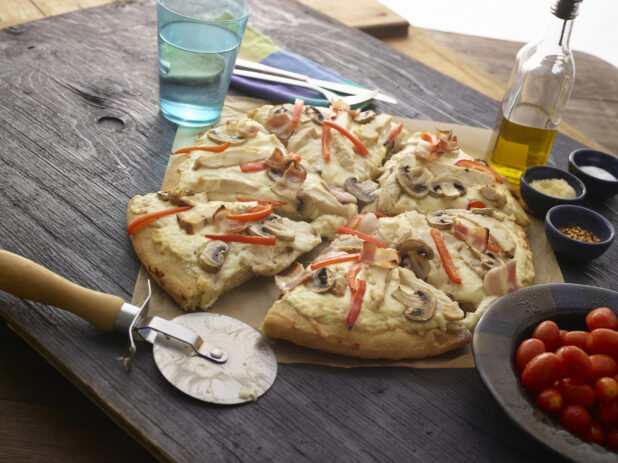 Sliced white pizza with mushrooms, red peppers, chicken, bacon and cheese on dark wooden background